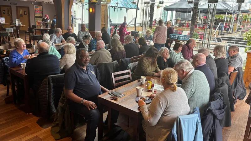A busy Brew and Banter social session at the Union Rooms in Plymouth, with around thirty people chatting over tea and coffee at wooden tables.