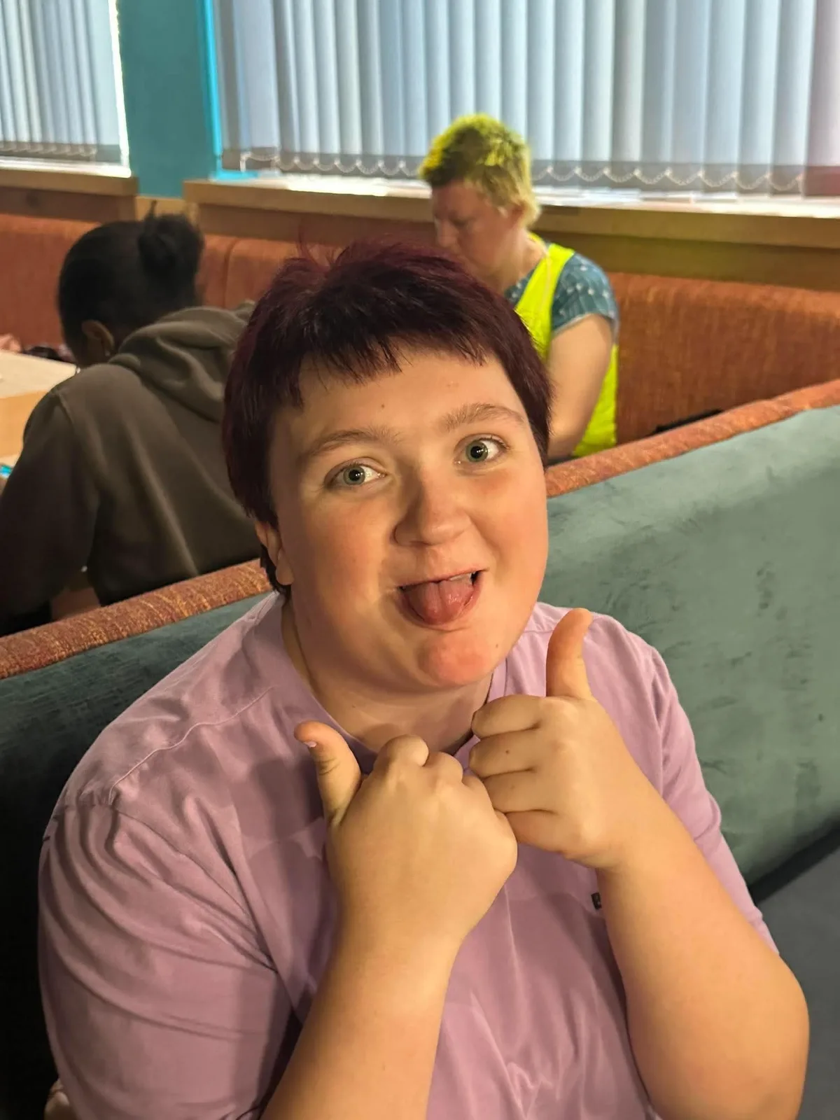 A guest in a lilac t-shirt sticks out her tongue and gives two thumbs up.