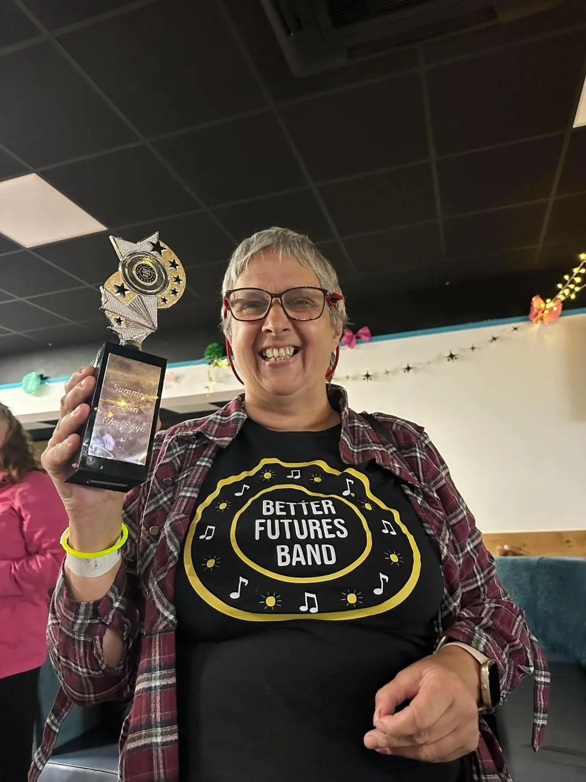 A beaming woman in a Better Futures Band t-shirt holds up the Summer Lovin’ Challenge trophy.